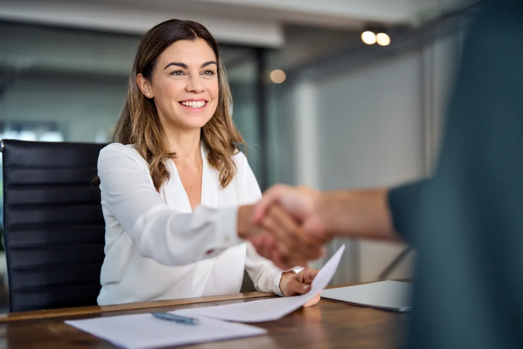 Image of a woman happily shaking the hand of person sitting across from a desk.